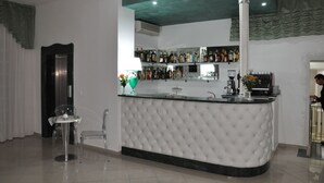 A bar area with a tufted white bar counter, a variety of liquor bottles, a coffee machine, and a clear glass bar stool. - Hotel Inn (Taormina)