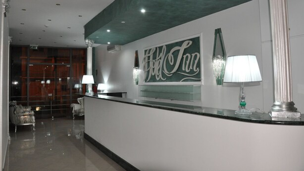 A reception area with a modern design, featuring a reception desk, a large wall sign, and a decorative lamp. - Hotel Inn (Taormina)