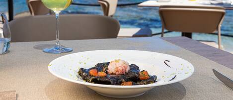 A dining table with a plate of seafood and a glass of white wine, overlooking the sea.