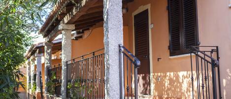 A building with a covered porch, stone columns, and a metal railing.