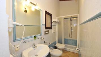 A bathroom with a sink, two toilets, a shower, and a hairdryer.