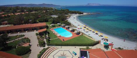 An aerial view of a resort with a swimming pool, beach, and ocean.