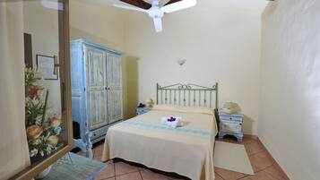 Une chambre à coucher comprenant un lit, une table de chevet, une commode, un ventilateur de plafond et un miroir.
