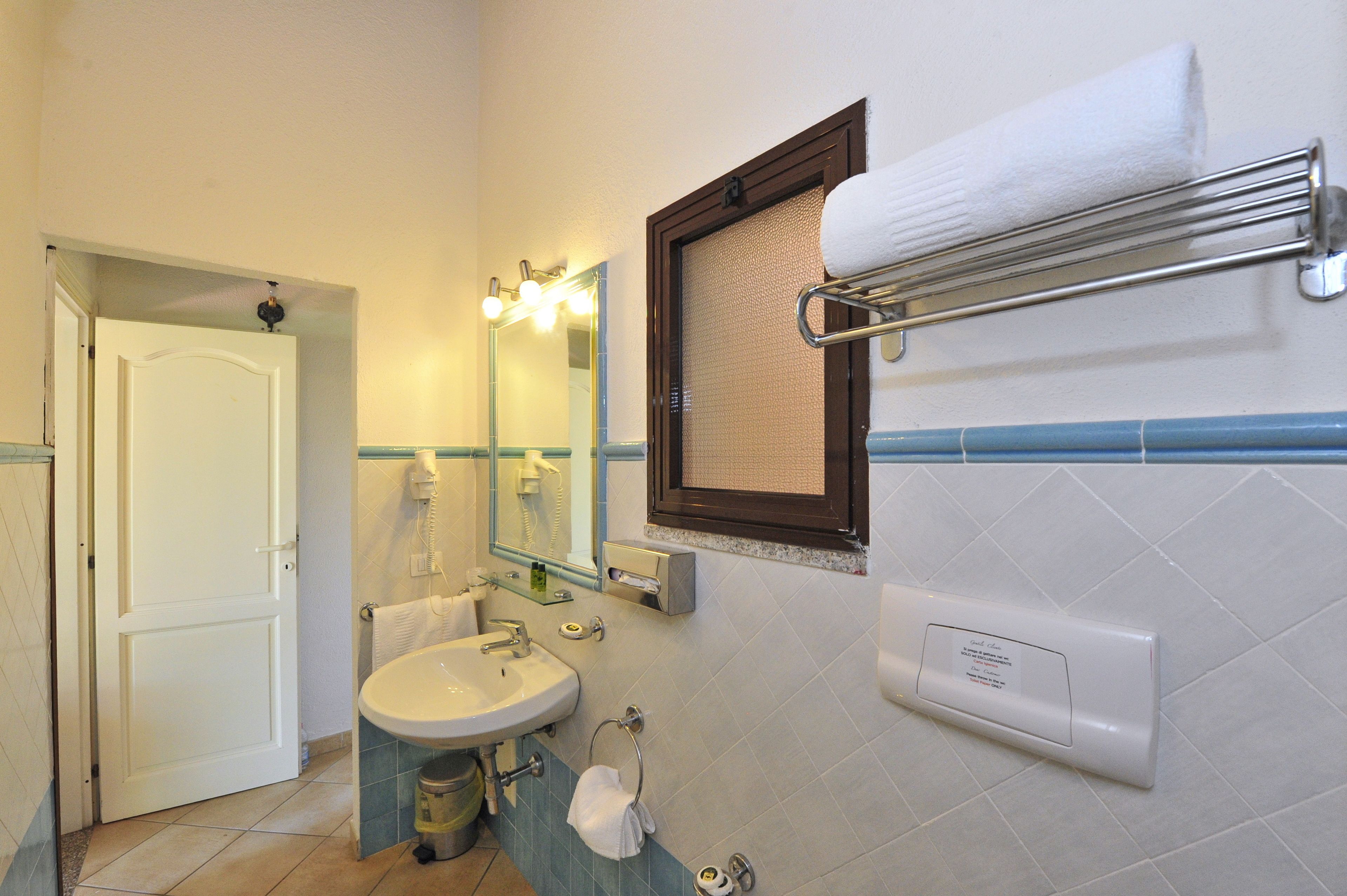Un baño con lavamanos, espejo, toallero y una puerta que da a otra habitación.