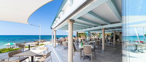 A covered outdoor dining area with tables and chairs, overlooking the sea.