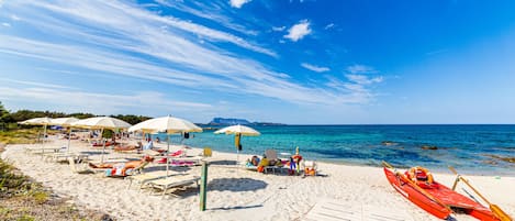 A beach with sun loungers, umbrellas, and a red canoe.