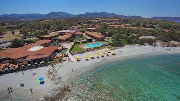 A coastal resort with a clear blue sea, a sandy beach, and a swimming pool.