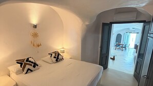 A bedroom with a large bed, a bedside table, and a wall-mounted light fixture. - Alta Vista Suites (Santorini)