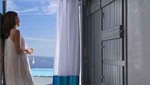 A woman standing by a door with a view of the sea. - Alta Vista Suites (Santorini)