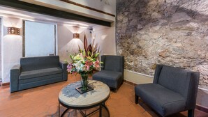 Eine Empfangshalle mit zwei Sofas, einem runden Tisch mit Blumen und einer Steinwand.