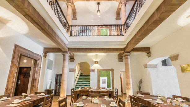 Ein geräumiger Essbereich mit Holztischen und -stühlen, ein Balkon mit schmiedeeisernem Geländer und eine Treppe, die in einen oberen Bereich führt.