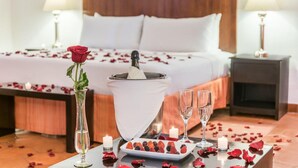 Ein ordentlich eingerichtetes Schlafzimmer mit einem Bett, Nachttischen, einer Nachttischlampe, einer Vase mit einer Rose, einer Schale mit Beeren und Kerzen.