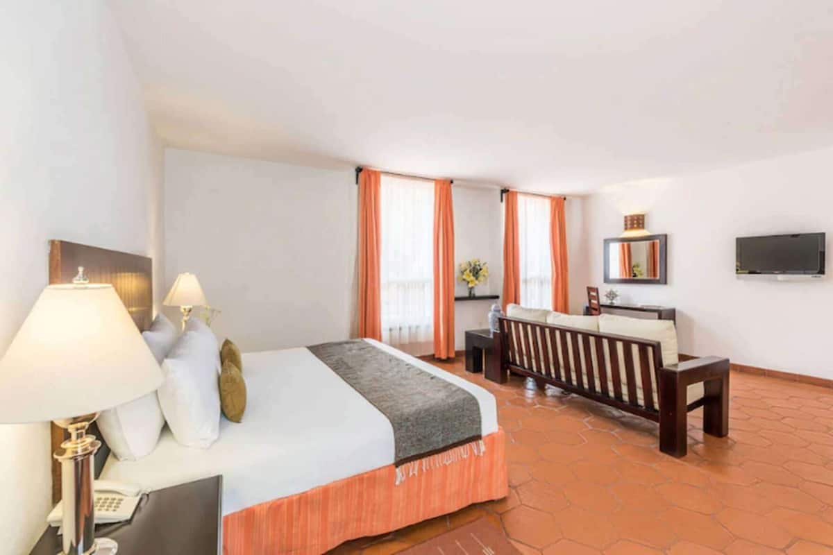 Une chambre d’hôtel équipée d’un lit, de lampes de chevet, d’un bureau, d’une chaise, d’une télévision et d’une fenêtre avec des rideaux.