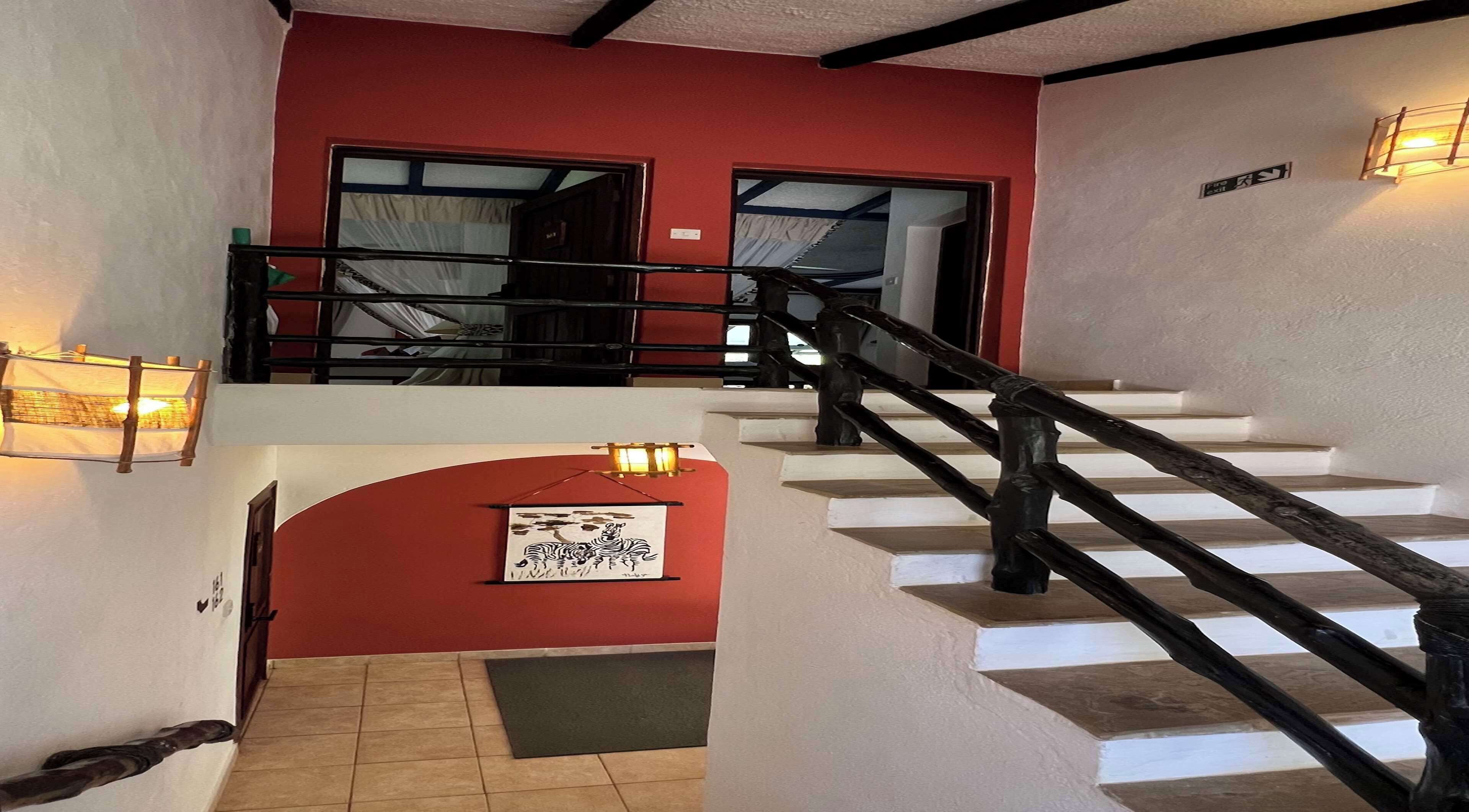 A staircase with a wooden handrail leading to a landing with a red wall and a framed picture.