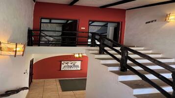 A staircase with a wooden handrail leading to a landing with a red wall and a framed picture.