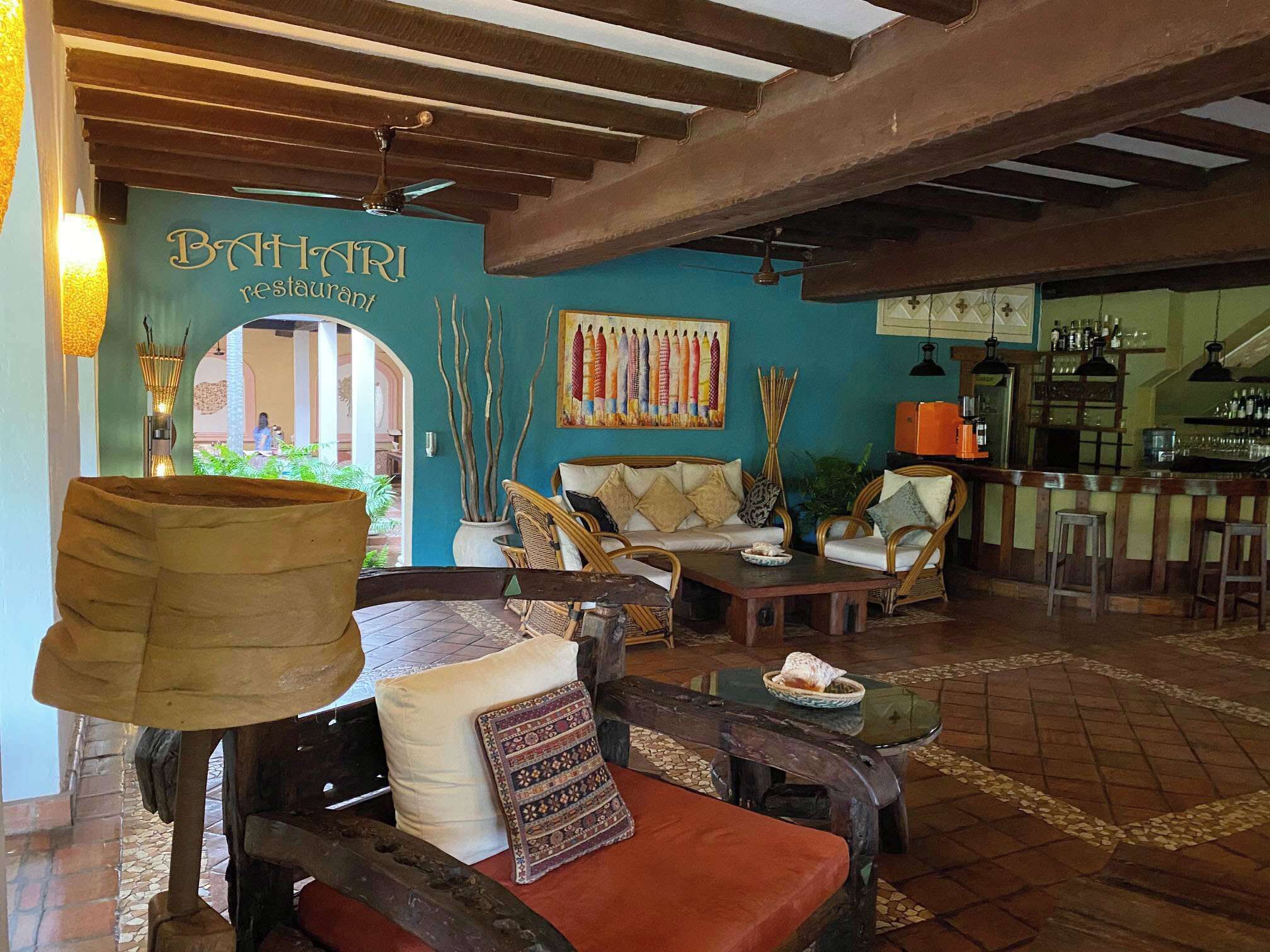 A restaurant interior with a bar area, wicker furniture, and a mural on the wall.