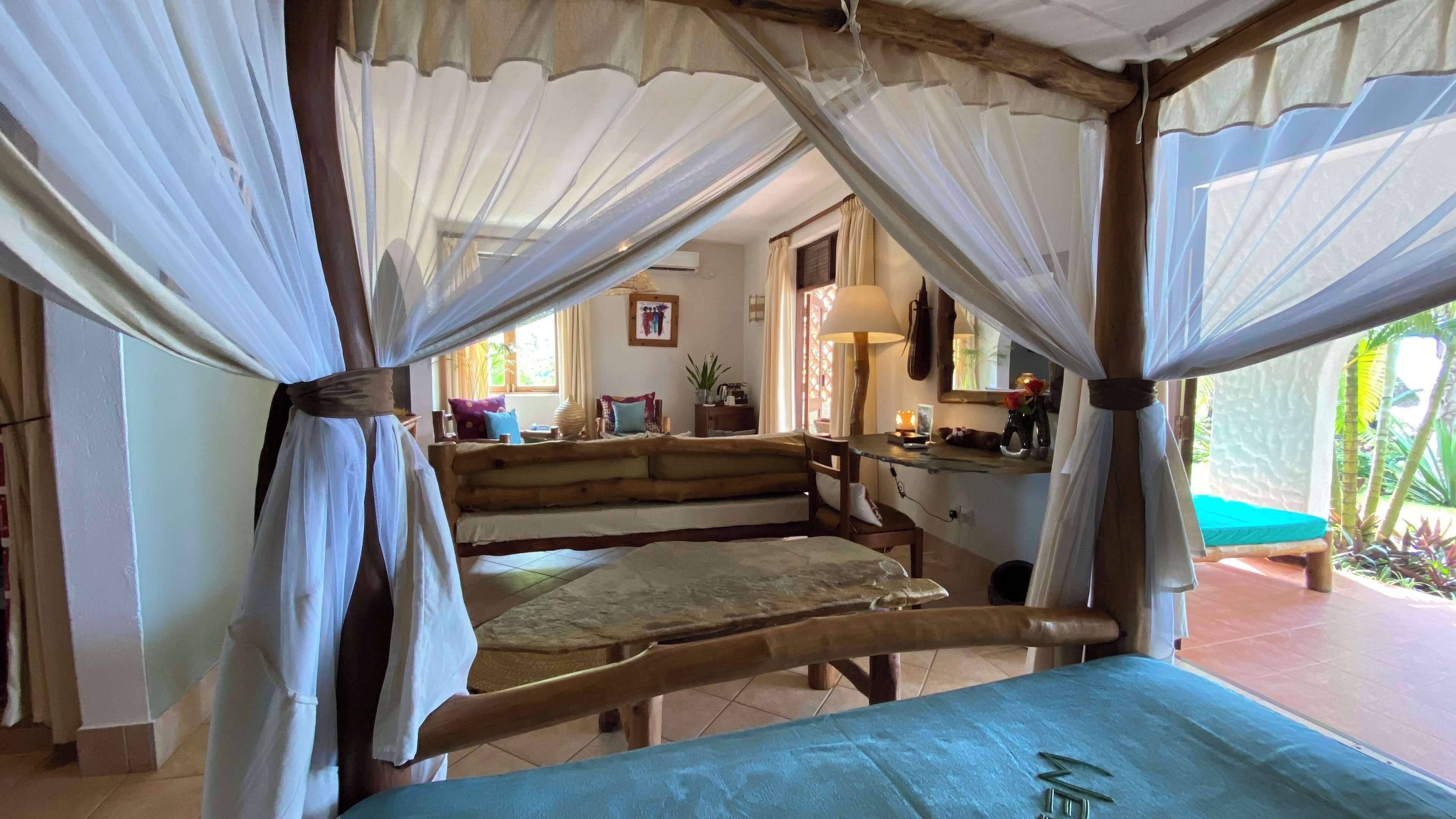 Una cama de madera rústica con dosel, una mesita pequeña y un banco en una habitación acogedora con vistas a un jardín.
