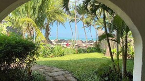 A tropical garden with a stone pathway leading to a beach view. - Neptune Palm Beach Boutique Resort & Spa All Inclusive (Diani Beach)