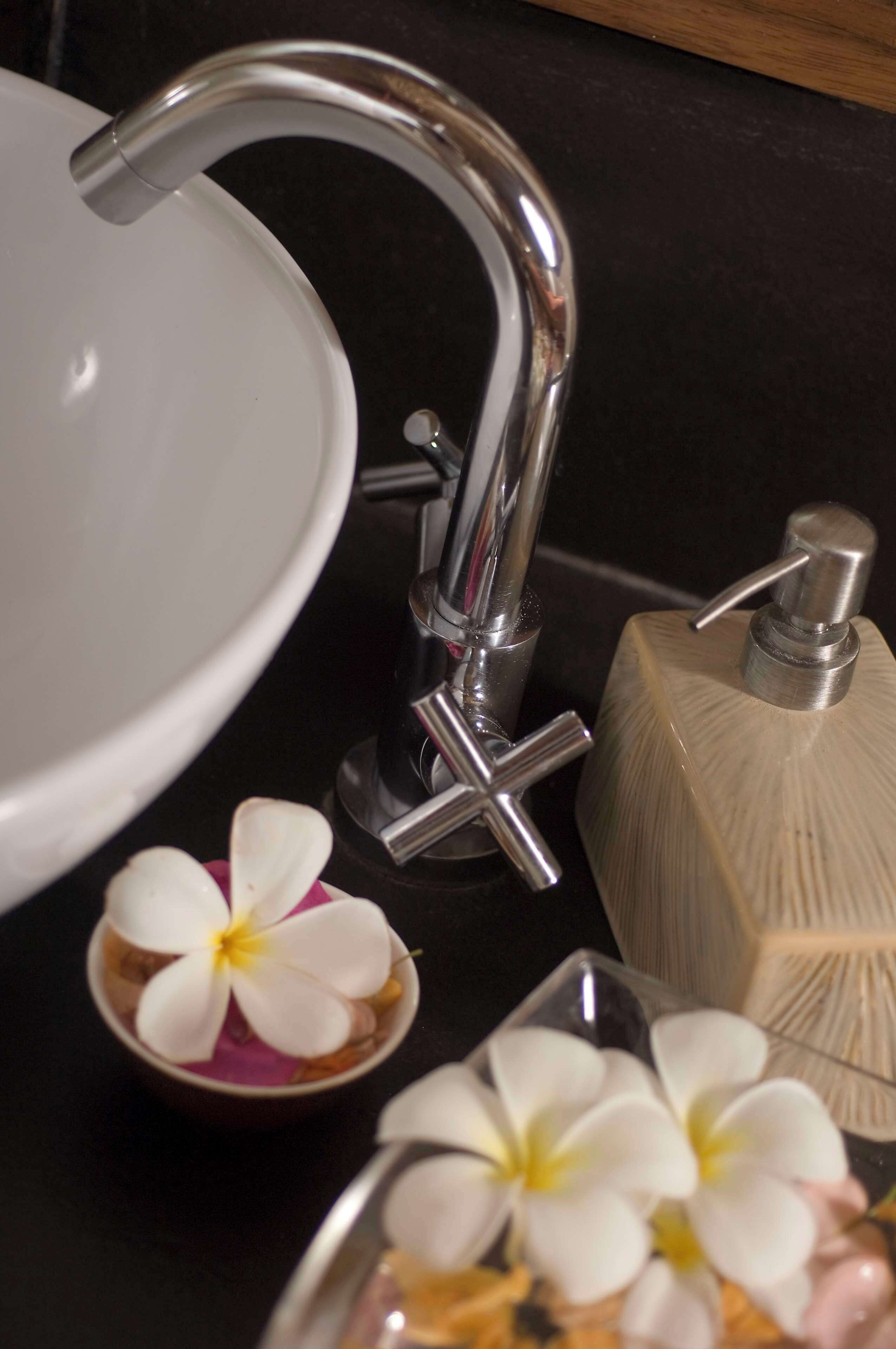 A bathroom sink with a chrome faucet, a soap dispenser, and a small bowl with white flowers.