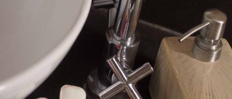 A bathroom sink with a chrome faucet, a soap dispenser, and a small bowl with white flowers.