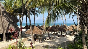 Una playa con sombrillas de paja, sillas de descanso y palmeras.