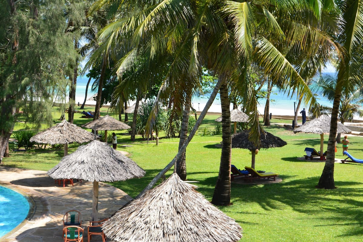 A pool area with thatched umbrellas, palm trees, and lounge chairs.