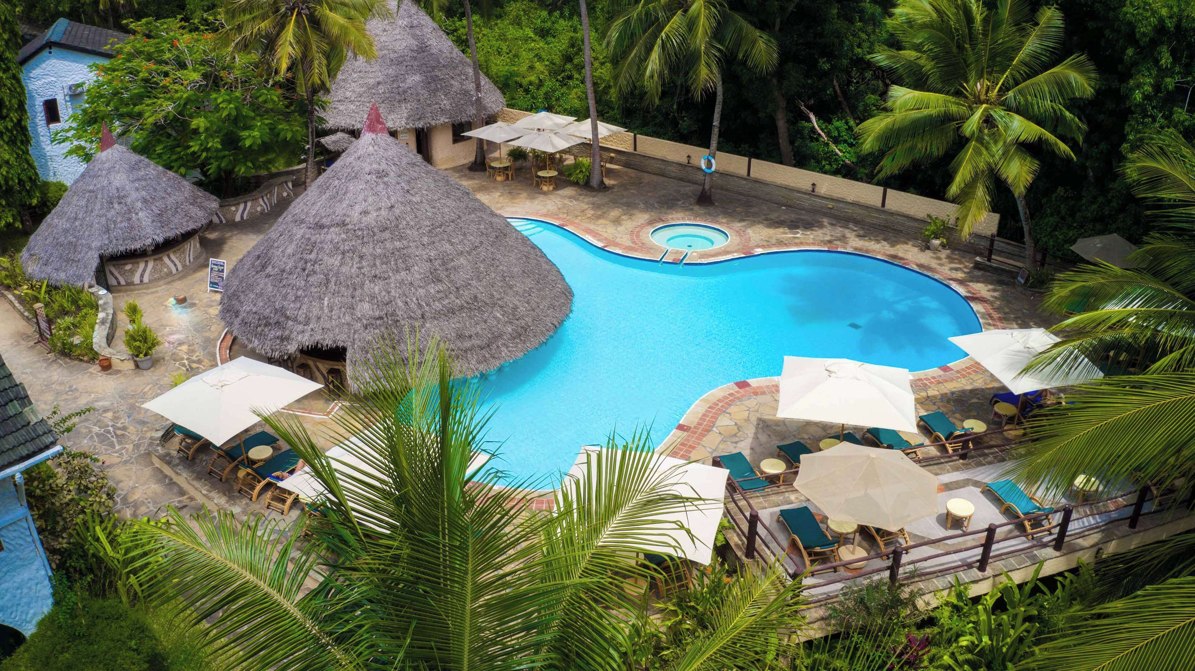 A resort with a central swimming pool, thatched-roof huts, and lounge areas with umbrellas.