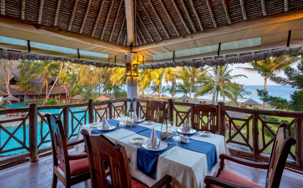 Un comedor con una mesa para dos, con vista a una piscina y una playa.