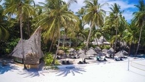 Un resort en la playa con cabañas de techo de paja, palmeras y una playa arenosa.