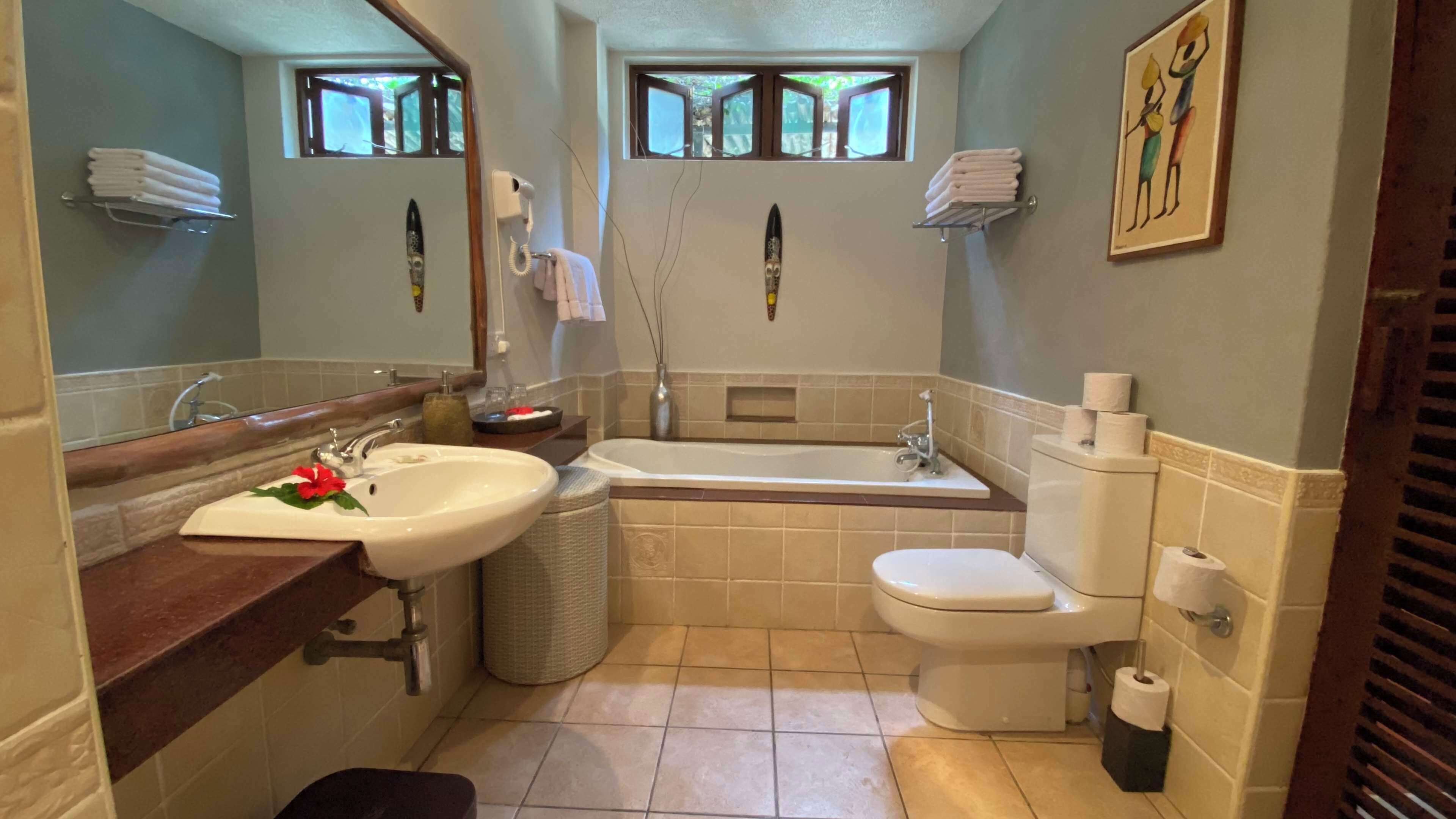 Une salle de bain avec un lavabo, des toilettes et une baignoire. Il y a des serviettes accrochées au mur et un tableau au-dessus des toilettes.