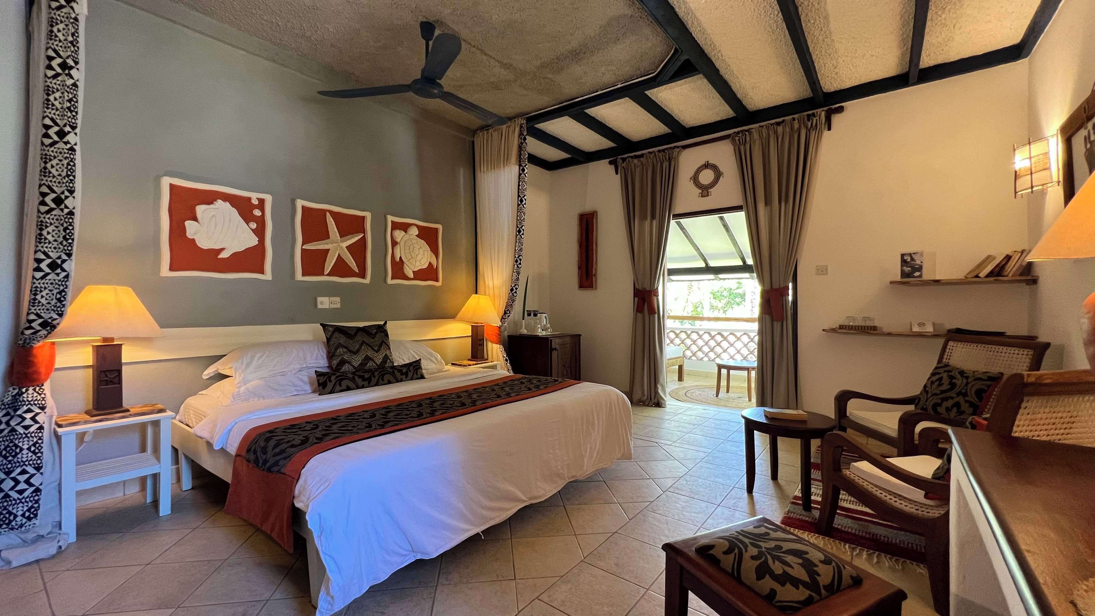 A hotel room with a bed, two bedside tables, a chair, a small table, and a ceiling fan.