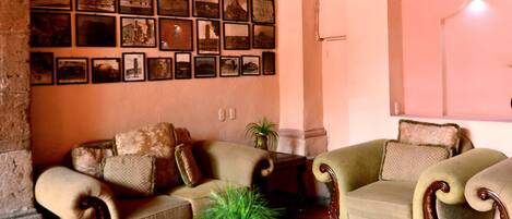 A cozy living room with a tiled floor, a wooden coffee table with a plant, two upholstered chairs, and a wall adorned with framed pictures.