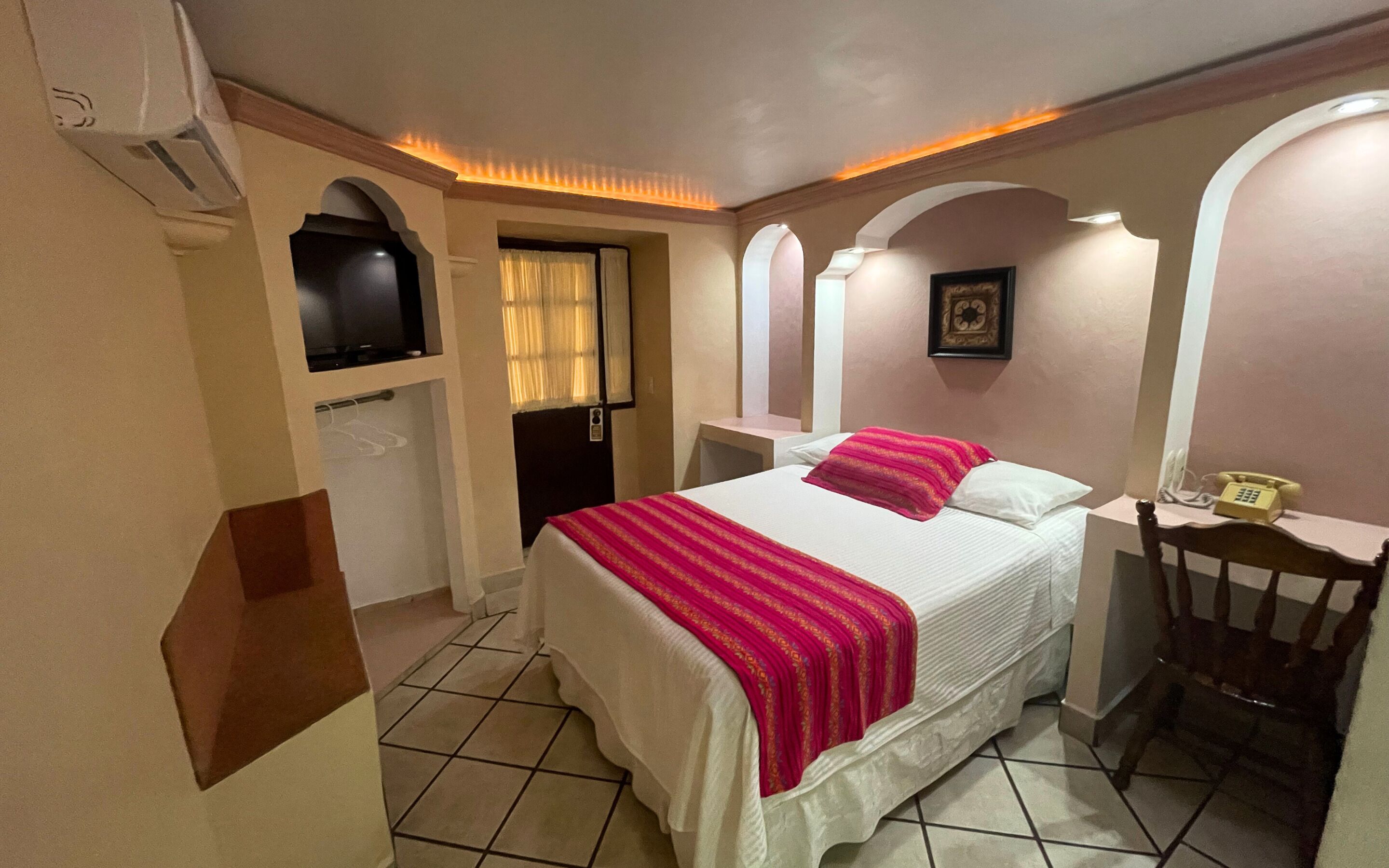 A hotel room with a bed, a desk with a telephone, and a TV mounted on the wall.