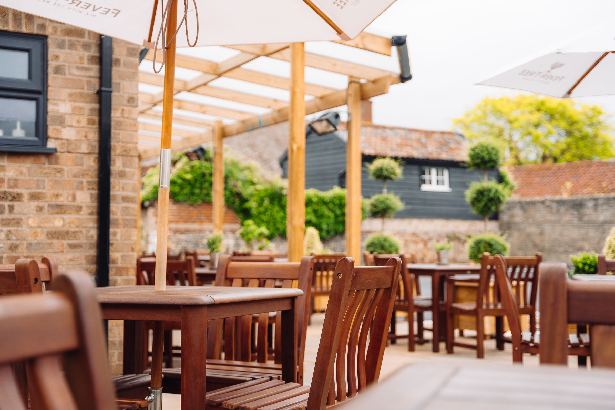 Un patio al aire libre con mesas y sillas de madera, un muro de ladrillo y una estructura de pérgola.
