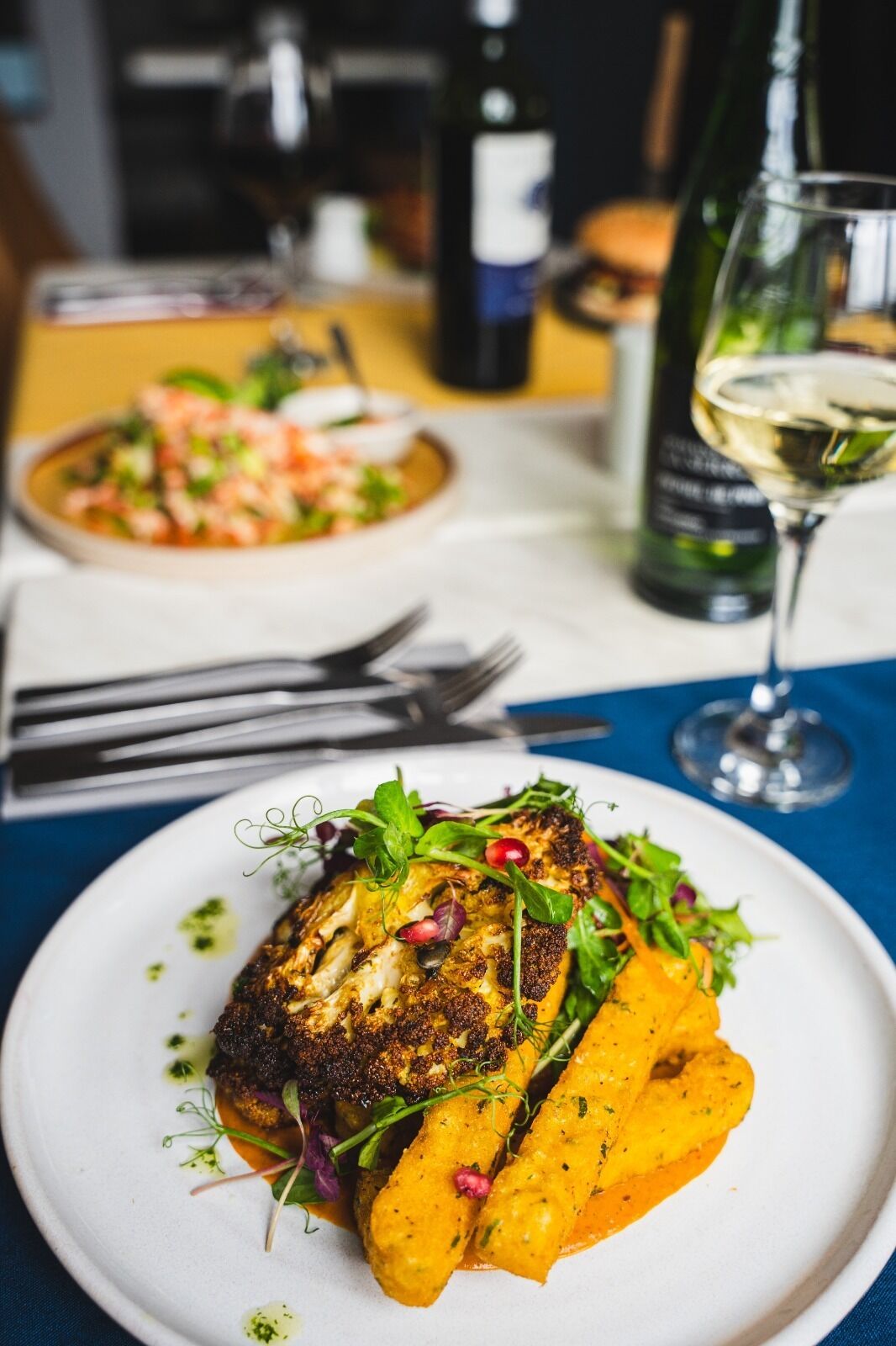 A dining table with plates of food, a wine glass, and a bottle of wine.