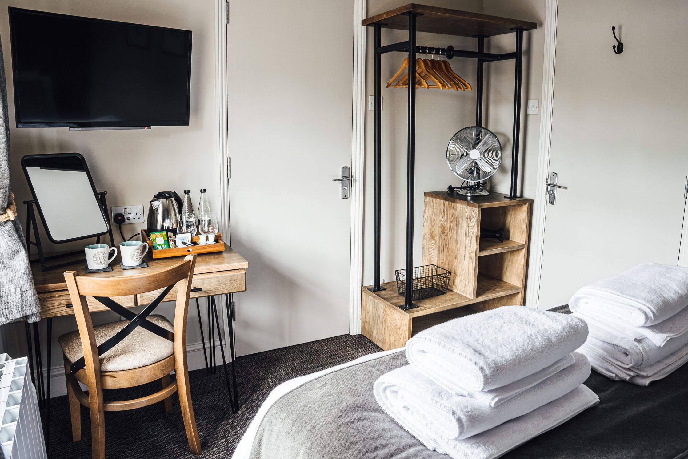 A hotel room with a bed, a desk with a computer, a chair, a TV, a fan, and towels.