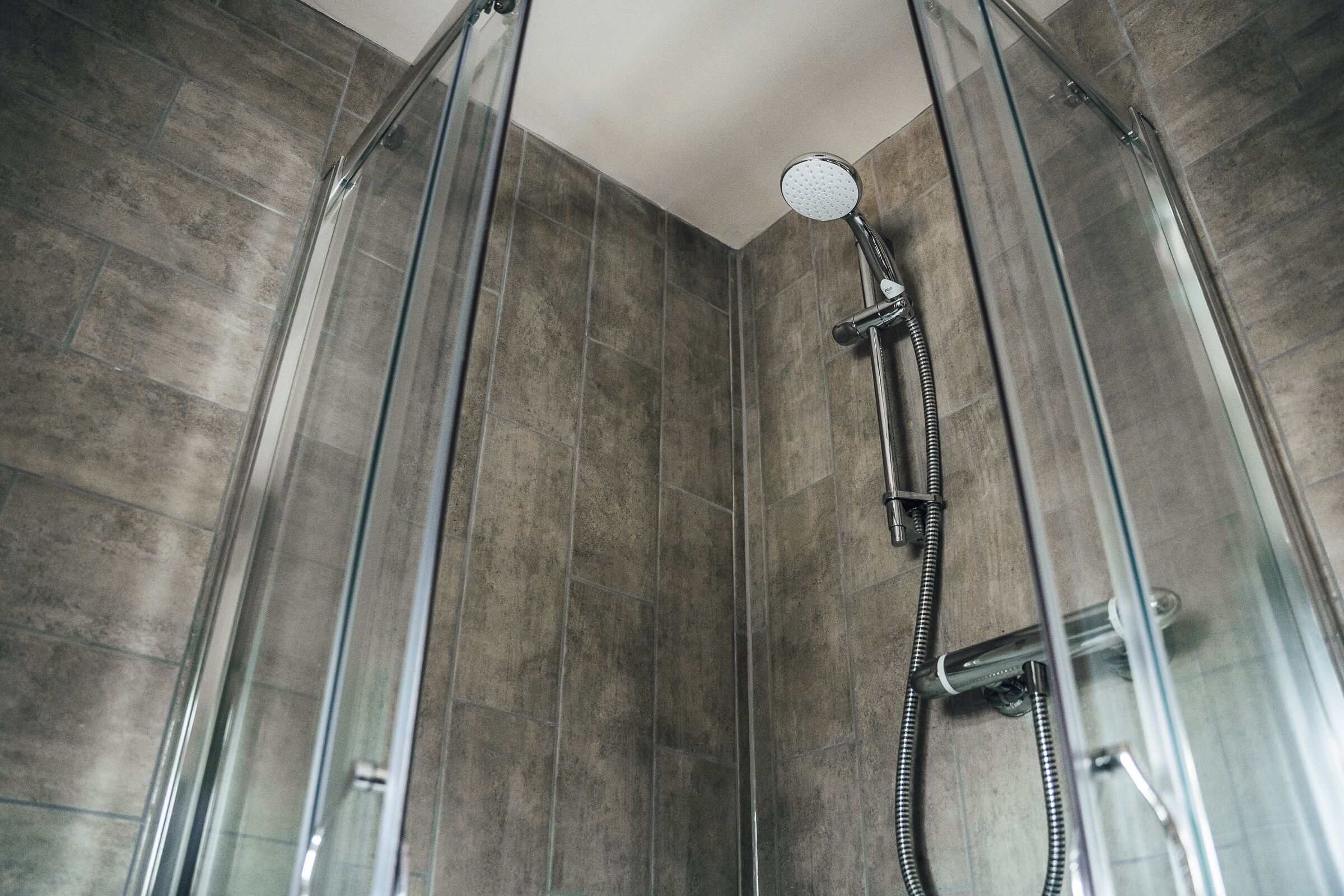 A glass-enclosed shower with a handheld showerhead and a hose.