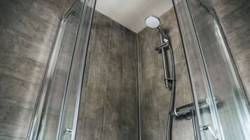 A glass-enclosed shower with a handheld showerhead and a hose.