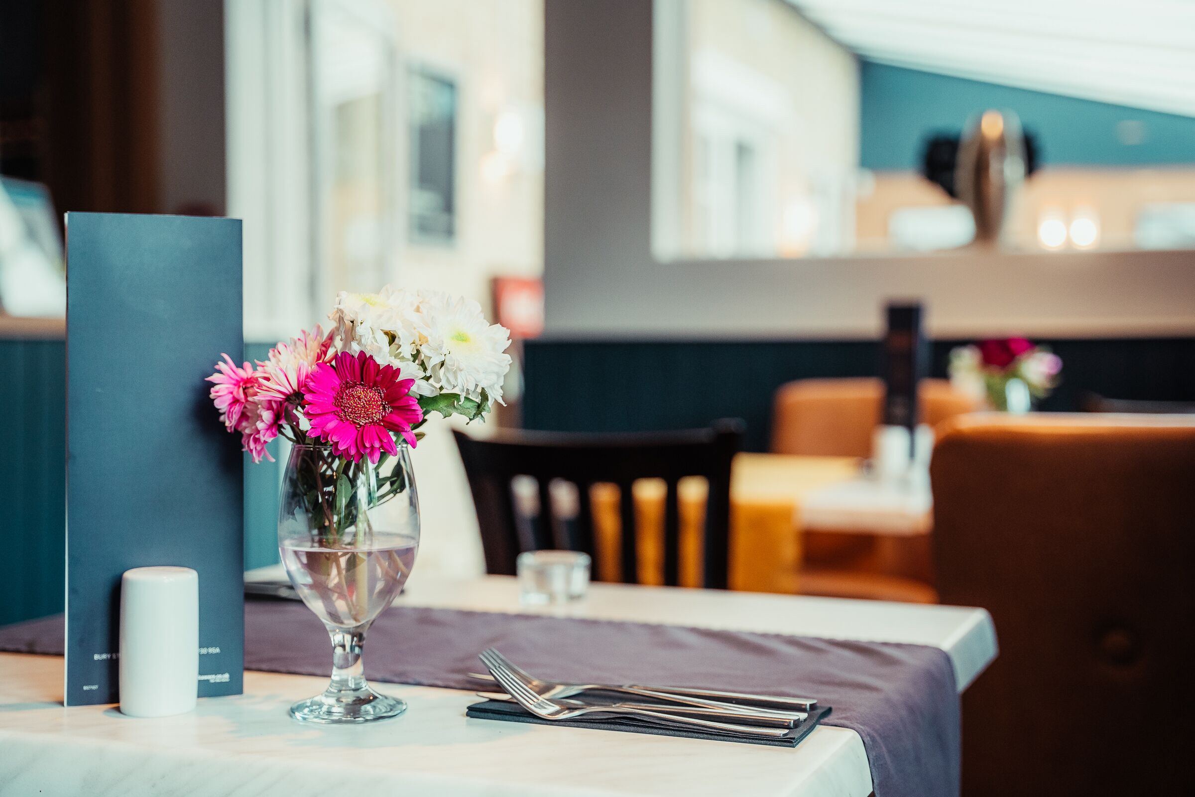 A dining table with a vase of flowers, a menu, and cutlery.