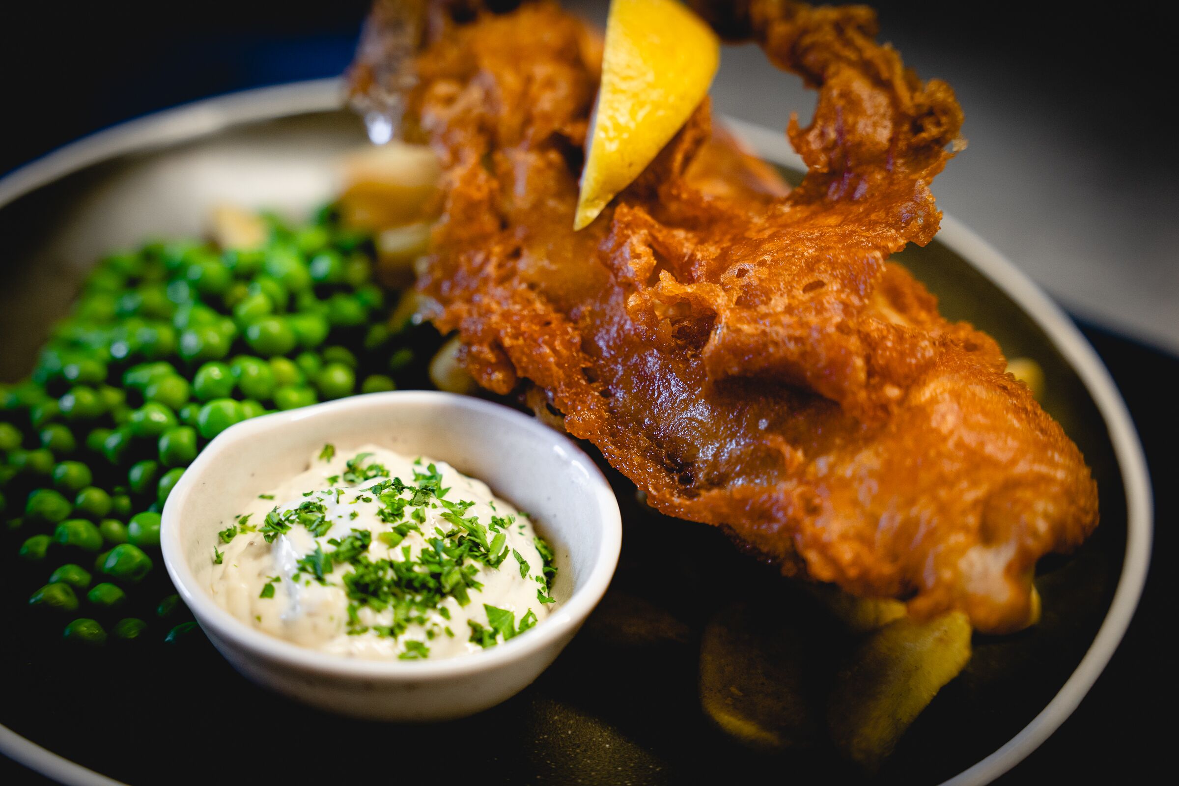 A plate with fried fish, peas, and a small bowl of sauce.