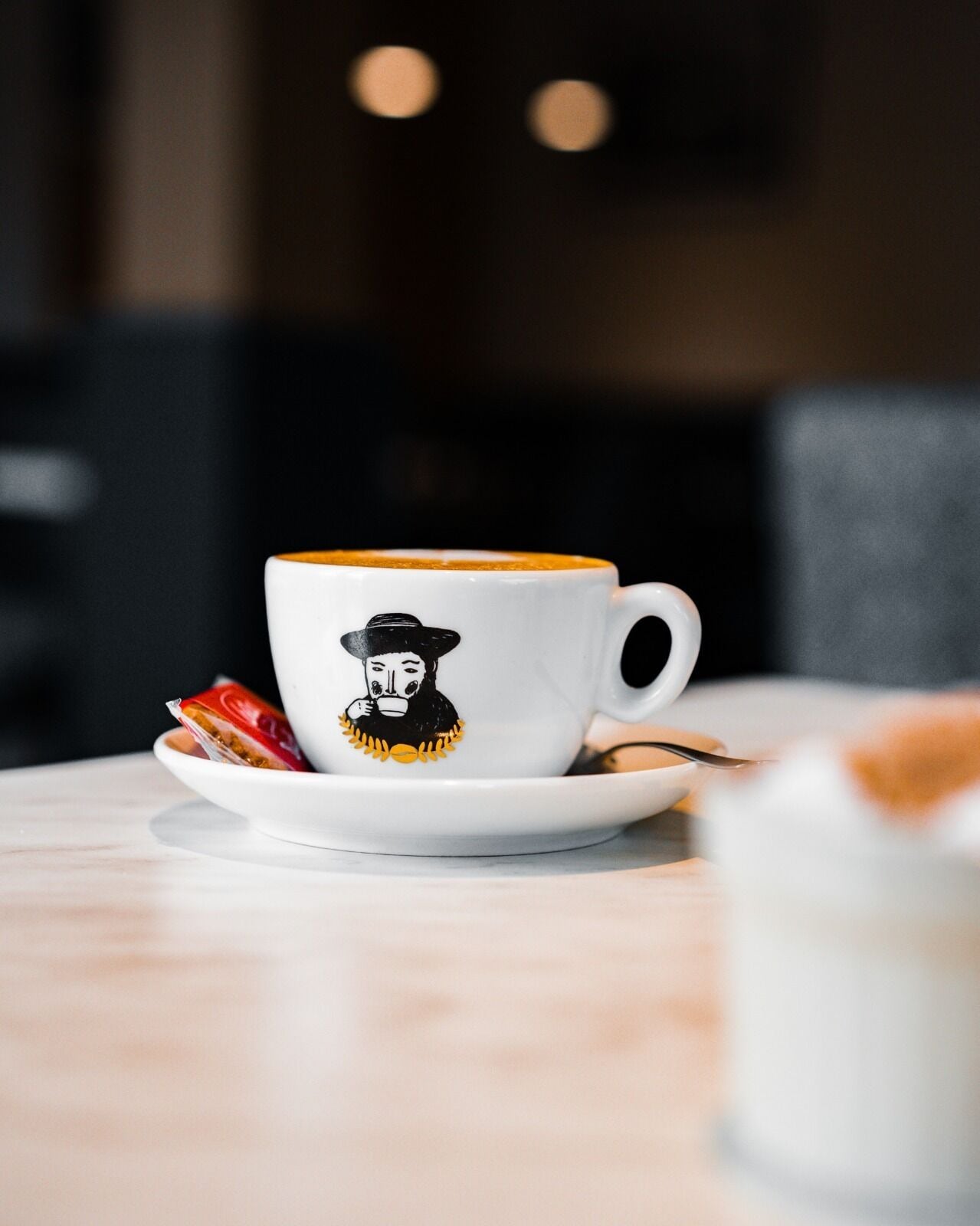 Una taza blanca con un diseño negro y amarillo sobre un platillo, colocada sobre una mesa.