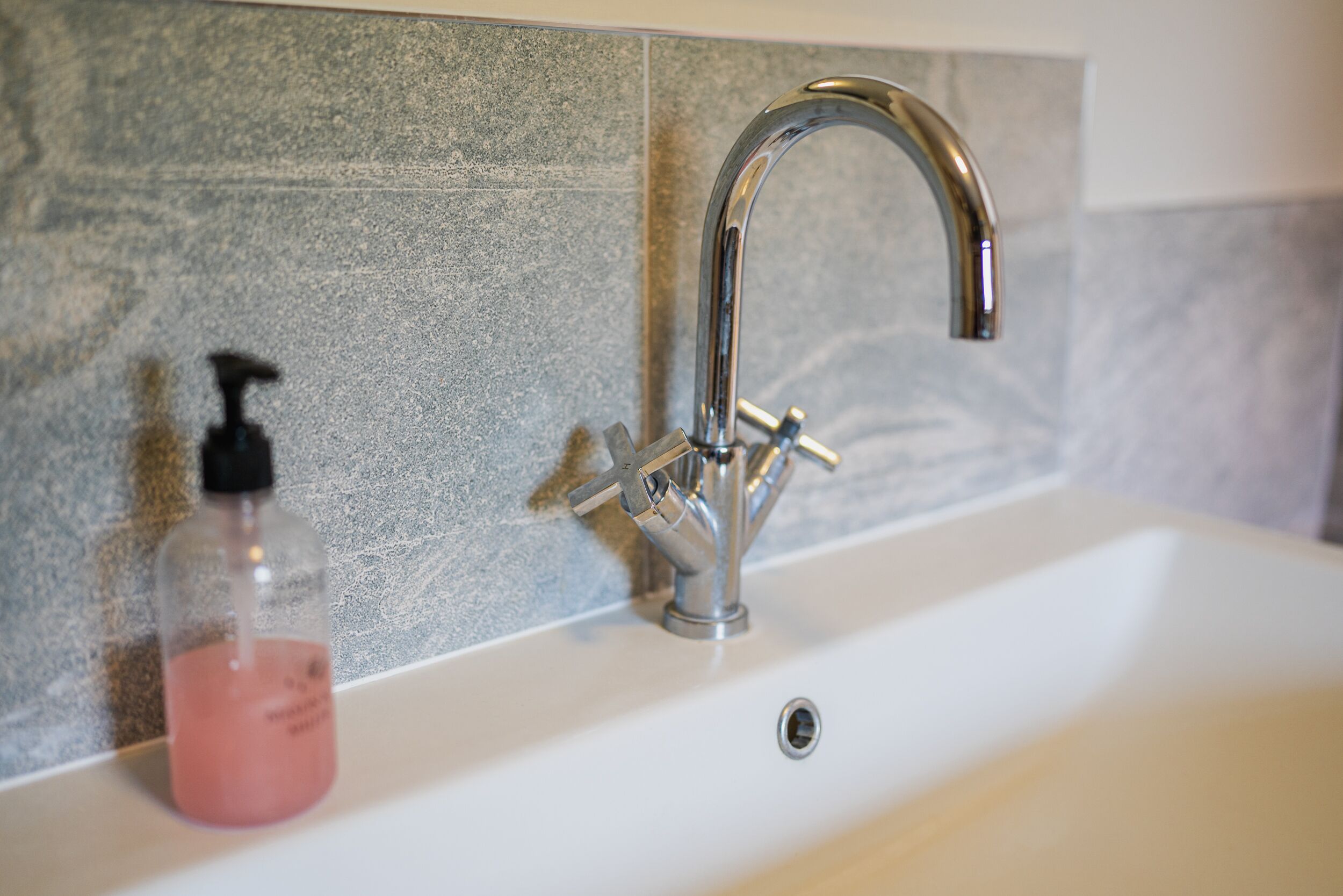 A bathroom with a modern sink, a faucet, and a soap dispenser.