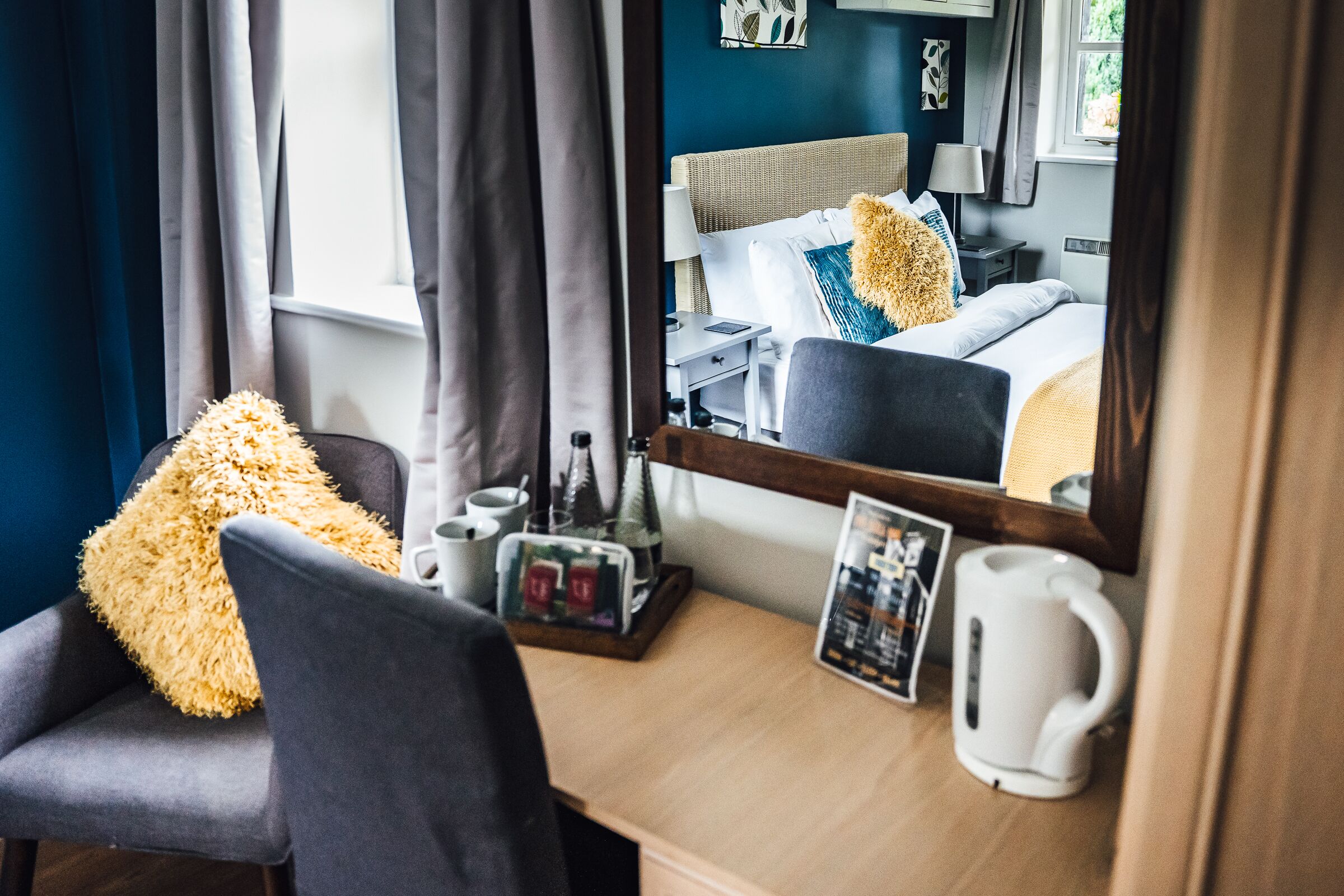 Ein Hotelzimmer mit einem Bett, einem Sessel, einem Schreibtisch mit Lampe, einer Kaffeemaschine und einem Bilderrahmen.