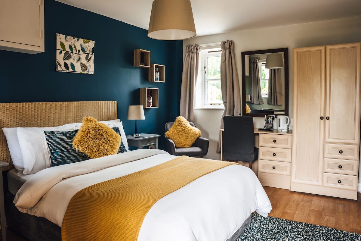 A bedroom with a bed, bedside tables, a desk, a chair, a wardrobe, and a window with curtains.