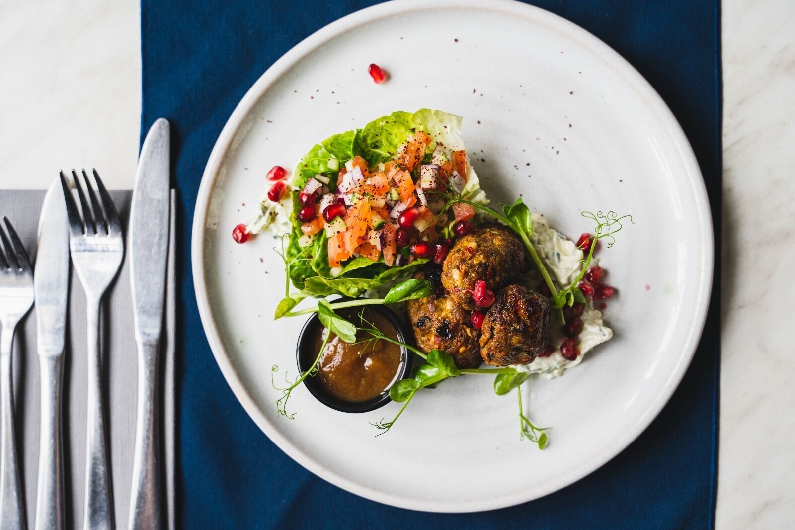 A plate with food, a fork, and a knife on a blue napkin.