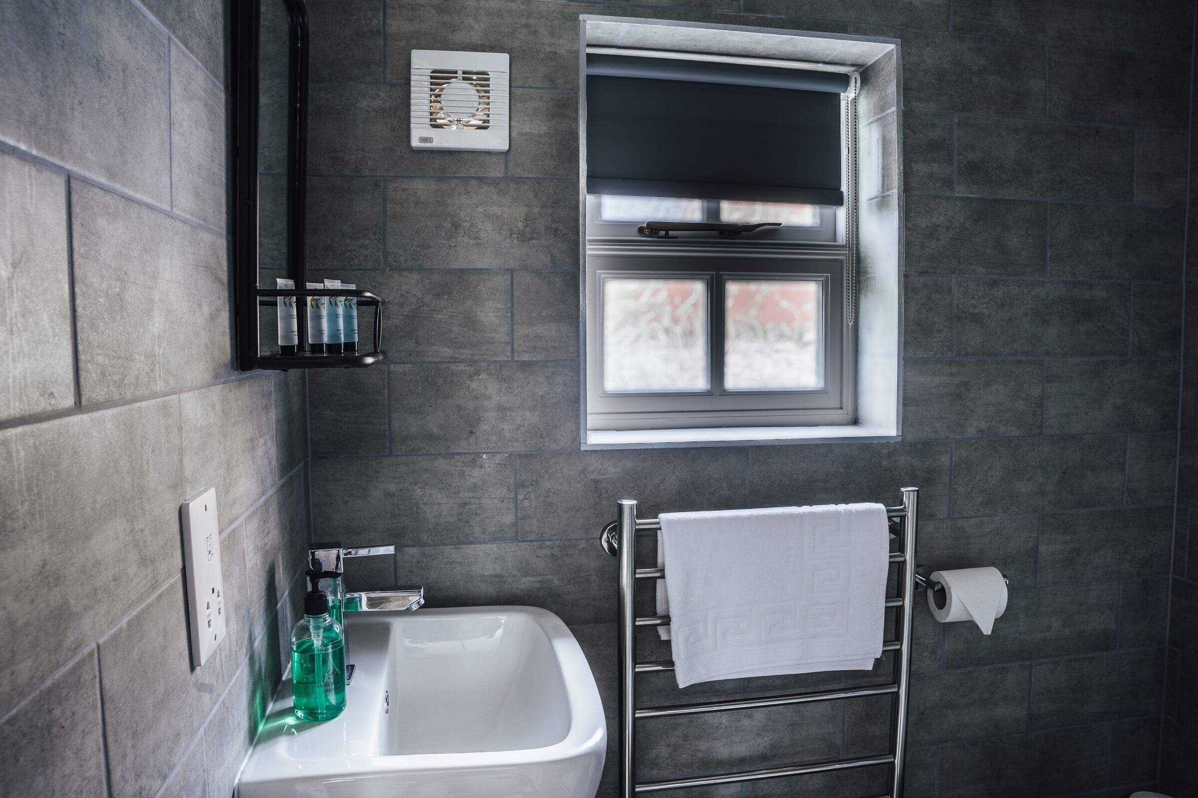A bathroom with a white sink, a towel rack with a white towel, a window, and a wall-mounted heater.