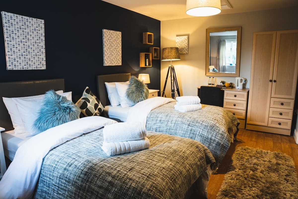 A modern bedroom with two beds, a wardrobe, a mirror, and artwork on the walls.