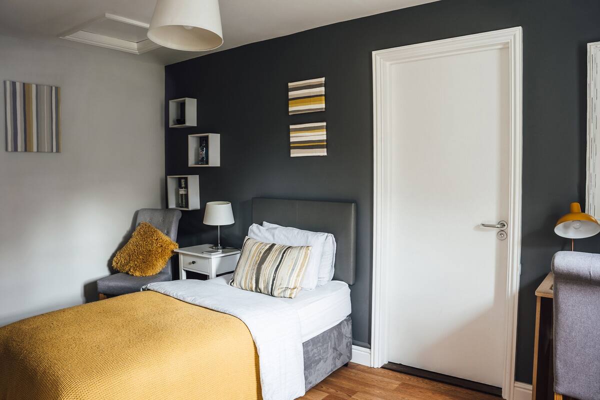 A modern bedroom with a bed, bedside tables, a chair, and a door.