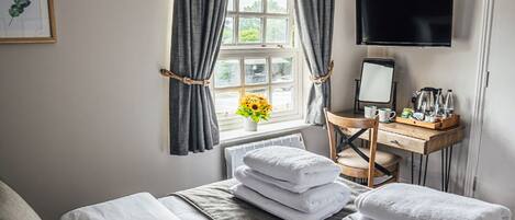 A hotel room with a bed, a desk with a chair, a TV, and a window with curtains.