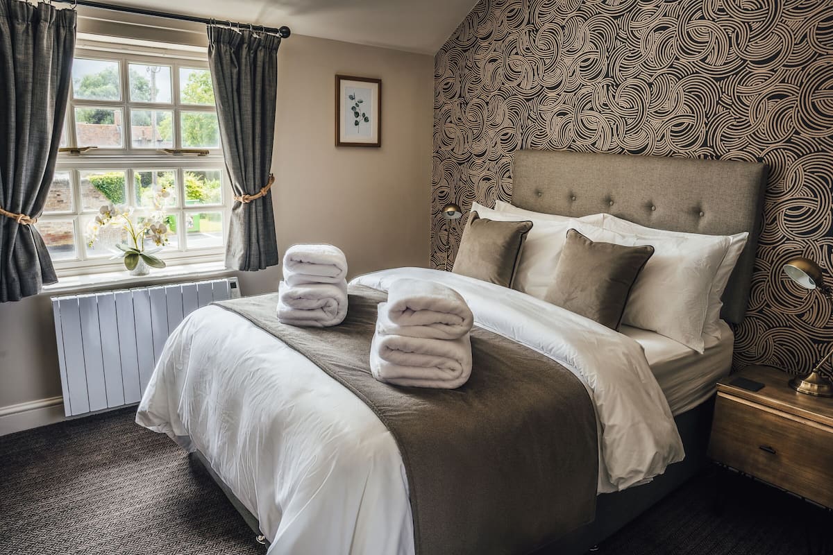 A neatly made bed with towels, a patterned wall, and a window with curtains.